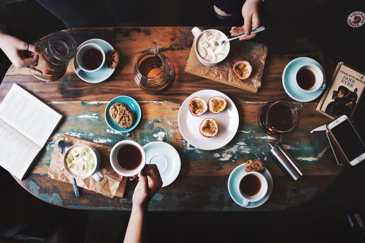 Friends sharing coffee, cups and a book across a rustic wooden table at Cafe Cebu